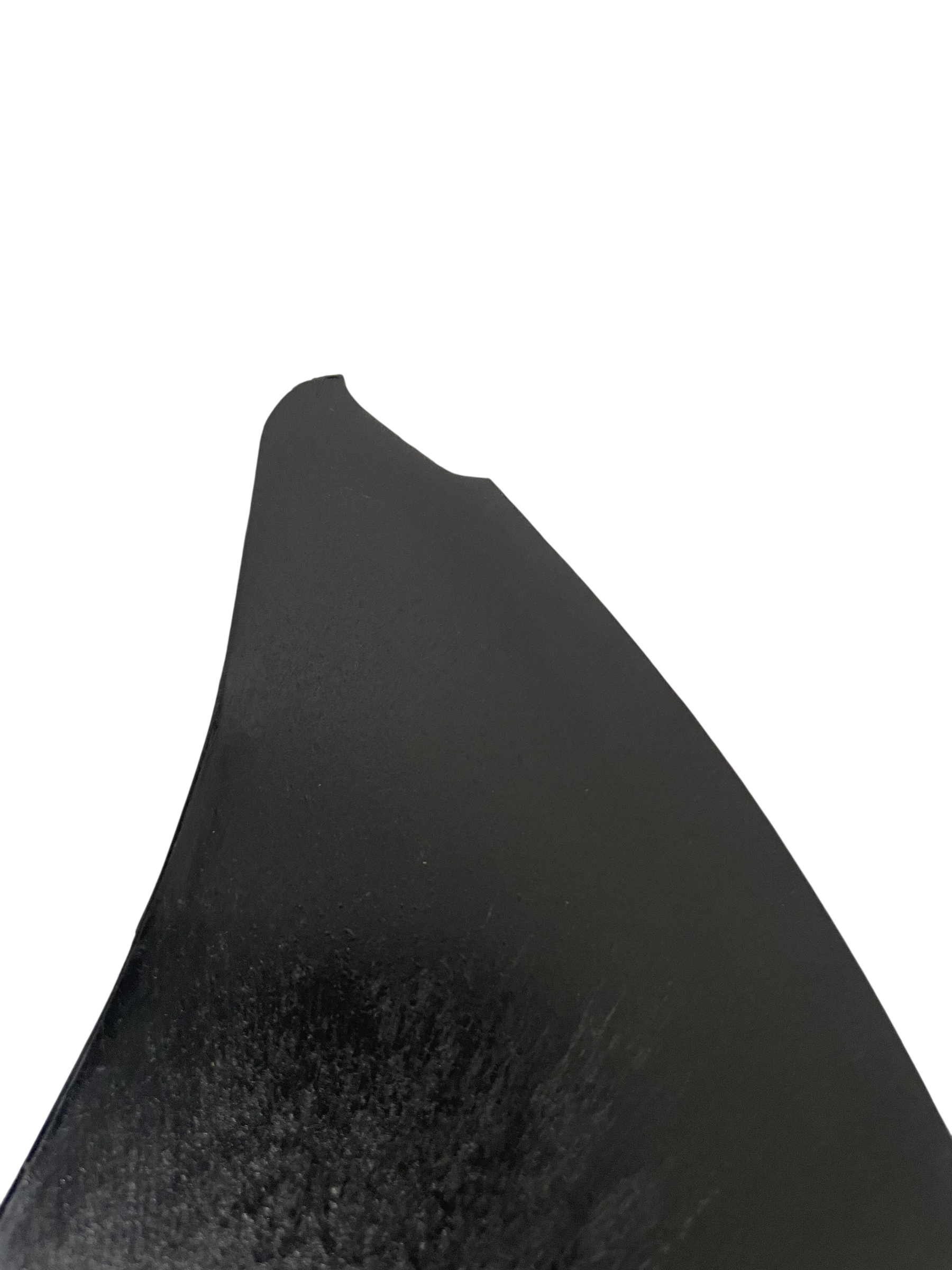 A close-up of a black curved object, possibly a piece of wood or a tool edge, against a solid white background.